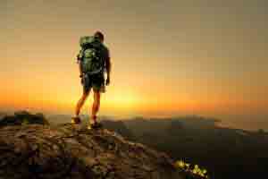 Hiker with backpack standing on top of a mountain and enjoying sunrise