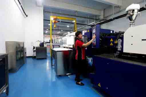 Worker operating plastic injection molding machine at Michigan CNC Machining Parts, Inc.